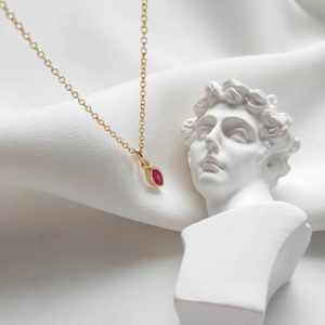 Detailed shot of a gold necklace featuring a marquise pink zircon on white silk fabric