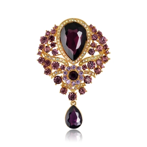 Vintage gold brooch with purple crystals and teardrop pendant on white background