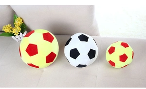 Three sizes of plush soccer ball pillows in red-yellow and black-white on a sofa