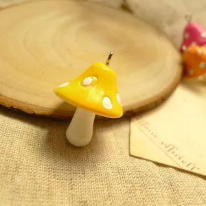 Detailed view of a yellow resin mushroom charm with white dots and a metal hook for DIY crafts