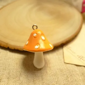Detailed view of an orange resin mushroom charm with white spots and a metal ring for DIY