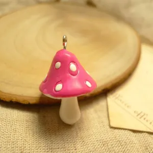 Macro detail of a small resin mushroom pendant with pink cap and white dots on a rustic base