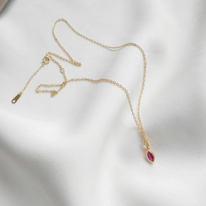 Close-up of gold necklace with marquise-cut pink gemstone pendant on white satin fabric