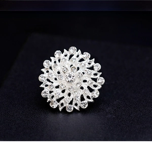 Detailed close-up of a silver flower brooch with crystal pavé on black texture