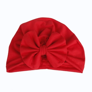 Detail view of baby turban hat featuring a large red bow and elastic cotton fabric