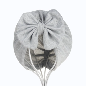 Gray cotton knit baby turban hat with a large bow detail shown on a product stand