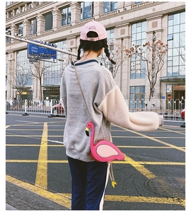 Back view of a person wearing a pink flamingo shaped crossbody chain bag in a city street