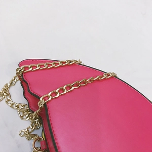 Close-up of rose red flamingo bag with gold metal chain strap on white marble surface