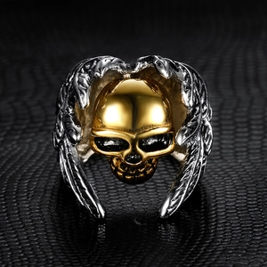 Detailed close-up of a gothic skull ring with golden face and silver wings on black leather