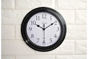 Detail of a 9-inch silent wall clock with black frame and 3D numeric dial on a white brick wall