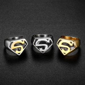 Three Superman S-shield rings in silver and gold tones on a textured black surface