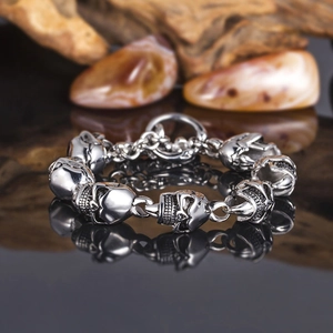 Polished silver skull link bracelet for men with reflection on dark glossy surface