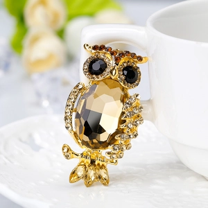 Luxurious gold-tone owl brooch with amber gemstone on a white ceramic coffee cup