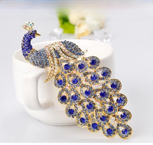 Macro detail of royal blue peacock brooch with crystals on white porcelain display