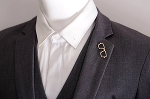 Close-up of a stylish gold glasses-shaped enamel brooch pinned on a men's suit lapel