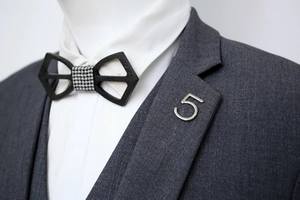 Detail view of a hollow wooden bowtie and number 5 metal brooch on a grey suit jacket