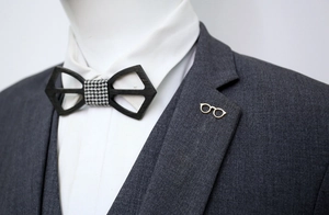 Detail of black wood cutout bowtie and gold sunglasses brooch on grey suit lapel