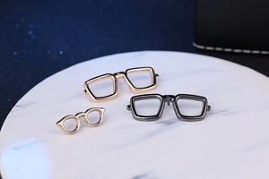 Close-up of enamel sunglasses brooches in gold and black on white marble surface