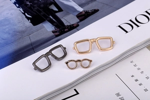 Detail of mini gold and gun black eyewear lapel pins displayed on a fashion magazine