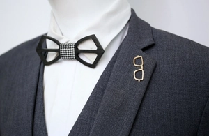 Detail of wooden bow tie with houndstooth center and gold eyewear shape lapel pin