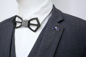 Detail view of blue glasses brooch and wooden bowtie on a grey suit jacket