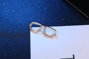 Close-up of a gold-toned metal eyeglasses brooch on a white card against a blue background