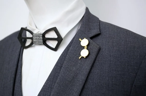 Detailed close-up of a gold glasses-shaped brooch on a dark grey suit lapel