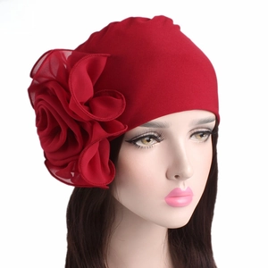 Detail of red elastic turban hat featuring a large layered chiffon side flower decoration