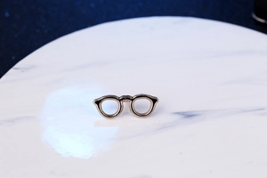 Detail of a golden sunglasses lapel pin on white marble plate for men suits