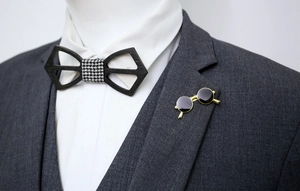 Detail of wooden bow tie and gold-framed enamel sunglasses brooch on a grey suit