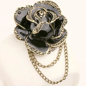 Detail of vintage black enamel rose brooch with rhinestones and bronze metal hanging chains