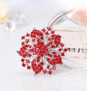 Close-up of luxury flower brooch with red crystals next to a perfume bottle