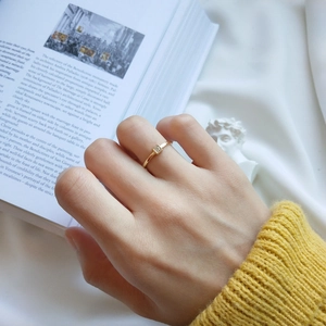 Detail of elegant gold thin ring with square gemstone worn by model against art book background