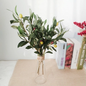 Artificial olive branches with green leaves and fruits in a rustic glass vase