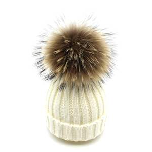 Détail du bonnet en tricot crème avec pompon en fausse fourrure brune et texture chaude