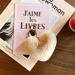 Close-up of a beige plush heart-shaped keychain with a gold metal ring on a pink background