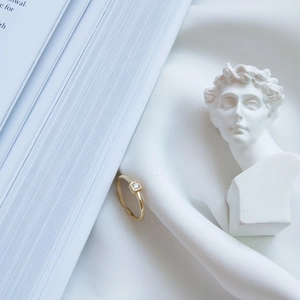 Detail of a minimalist gold square zircon ring on white silk with plaster bust