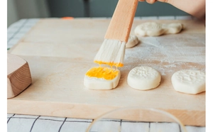 Detail of wooden pastry brush applying egg wash onto mooncakes on a rustic board