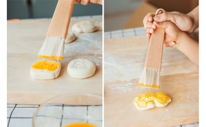 Detail of beech wood pastry brush applying egg wash on pastries over a wooden board