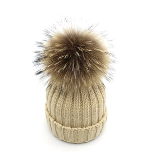 Texture détaillée du bonnet en tricot beige avec un grand pompon moelleux en fourrure