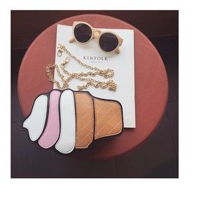 Flat lay of an ice cream cone shaped crossbody bag with gold chain and chic props