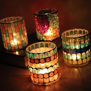 Set of four colorful mosaic glass candle holders with warm light on a wooden table