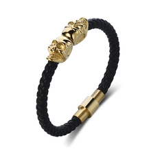 Detail of woven leather magnetic bracelet featuring gold skull charms and cylinder clasp