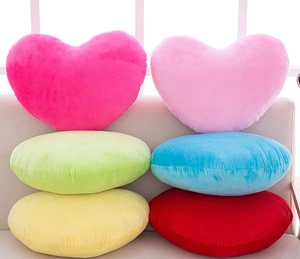 Close-up of colorful heart and round plush pillows on a soft beige sofa in bright light