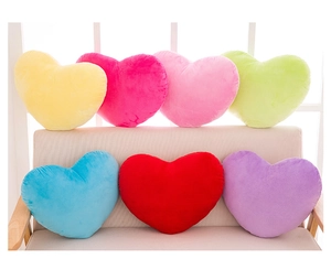 Colorful heart-shaped plush pillows in seven vibrant colors arranged on a beige sofa