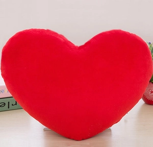 Close-up of soft red heart-shaped plush pillow on a wooden desk with a minimalist background