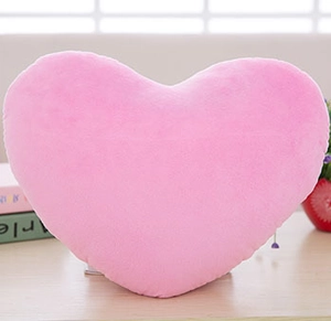 Primo piano di un morbido cuscino di peluche a cuore rosa su sfondo decorativo interno
