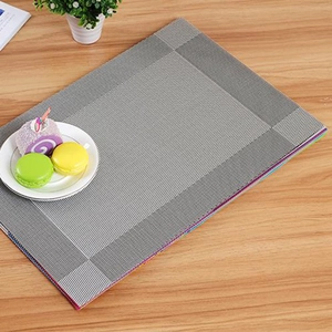 Gray rectangular woven PVC placemat with fine texture on a wooden dining table
