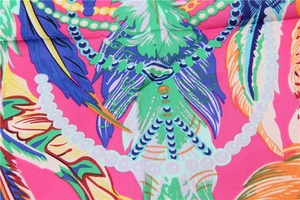 Détail du foulard en soie avec motifs plumes et perles colorées sur tissu rose vif