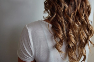 Detailed back view of a woman with long wavy brown hair styled using a foam hair roller